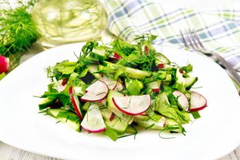 Salad of radish, cucumber, sorrel and greens, dressed with vegetable oil in a plate on the background of wooden board