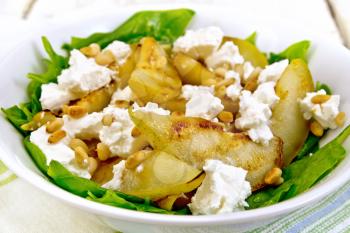 Salad of fried pear, spinach, salted feta cheese and cedar nuts in a plate on a kitchen towel against a light wooden board