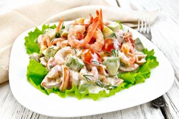 Salad with shrimp, avocado, tomatoes and mayonnaise on the green lettuce in a white plate, apkin, fork on the background of wooden boards