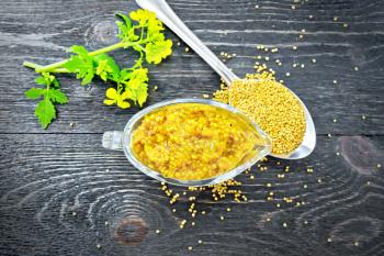 Mustard Dijon sauce in a glass sauceboat, yellow flowers and mustard seeds in a spoon on a wooden board background from above