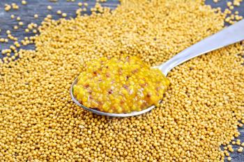 Mustard Dijon sauce in a metal spoon on the seeds on wooden board background