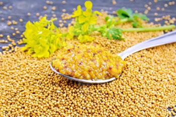 Mustard Dijon sauce in a metal spoon and yellow mustard flower on the seeds on wooden board background
