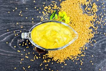 Mustard sauce in a glass sauceboat, seeds and flowers of mustard on the background of a wooden board from above