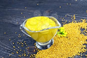 Mustard sauce in a glass sauceboat, seeds and flowers of mustard on the background of a wooden board