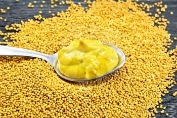Mustard sauce in a metal spoon on mustard seeds against the background of a wooden board