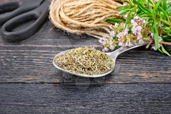 Thyme dry in a metal spoon, a bunch of fresh herbs with flowers, a skein of twine and scissors on a wooden plank background