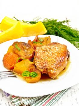Chicken stew with pumpkin, dried apricots, carrots and red wine, sprinkled with sesame seeds in a plate on a napkin, fork and dill against light wooden board