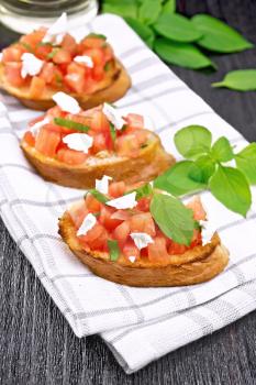 Bruschetta with tomato, basil and soft cheese on a napkin on dark wooden board