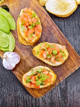Bruschetta with tomato, basil and spinach on a plate, garlic and fresh green leaves on a wooden board background from above
