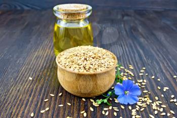 Linen seeds are white in a bowl, linseed oil in a glass jar and blue flax flower on a wooden board background