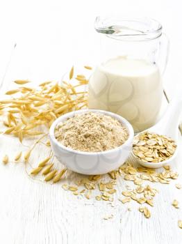 Flour oat in bowl, milk in a jug, oatmeal in spoon, oaten stalks on the background of light wooden table