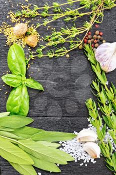 Frame of savory leaves, basil, sage and thyme, salt, nutmeg, mustard seeds, pepper and garlic on the background of wooden boards
