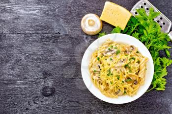 Fusilli pasta with champignons in creamy sauce, parsley and grated cheese in a plate on wooden board background from above