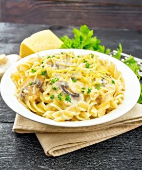 Fusilli pasta with champignons in creamy sauce, parsley and grated cheese in a plate on napkin on black wooden board background
