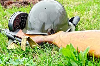 A helmet and a submachine gun of the times of the Great Patriotic War, a bag of protective color against the background of green grass