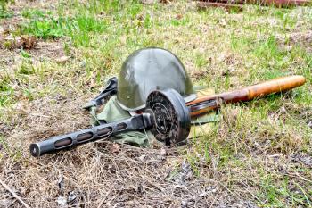 A helmet and a submachine gun of the times of the Great Patriotic War, a bag of protective color against the background of grass