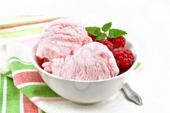 Ice cream crimson with raspberry berries and mint in white bowl, a spoon on towel on the background of light wooden board