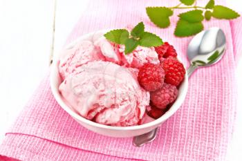Ice cream crimson with raspberry berries and mint in white bowl, a spoon on pink napkin on wooden board background