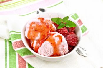 Ice cream crimson with raspberry berries, syrup and mint in white bowl, a spoon on napkin on light wooden board background