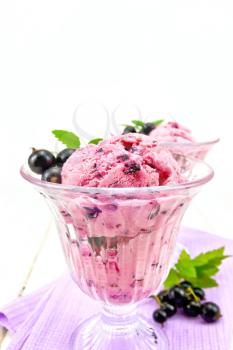 Ice cream with black currant in two glasses on a napkin, berries with leaves on a wooden board background