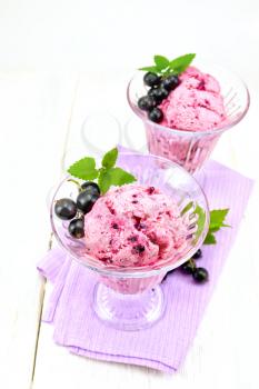 Ice cream with black currant in two glasses on a lilac napkin, berries with leaves on a wooden plank background
