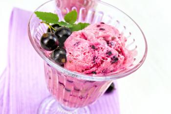 Ice cream with black currant in a glass goblet on a lilac napkin, berries on a wooden plank background