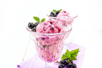 Ice cream with black currant in two glasses on a napkin, berries with leaves against a light wooden board