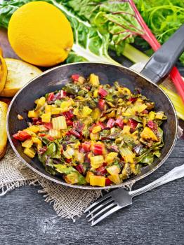 Warm chard salad with orange and onion in an old frying pan on sackcloth, bread, fork on a black wooden board background