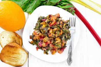 Warm chard salad with orange and onion in a plate, bread, fork on a wooden board background from above