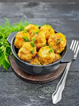 Meatballs with tomato sauce in a brazier with parsley, dill, fork on a wooden plank background