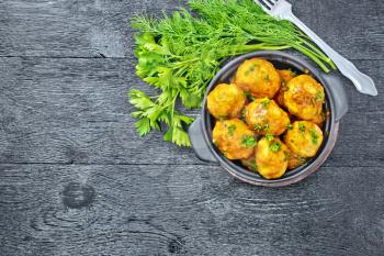Meatballs with tomato sauce in a black brazier with parsley, dill, fork on a wooden plank background on top