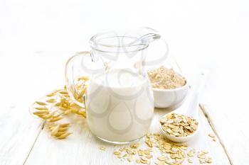 Oat milk in a jug, flour in bowl, oatmeal in spoon, stalks oaten on a wooden board background
