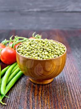 Green lentils mung in a bowl, pods of beans and red tomatoes on the background of a dark wooden board