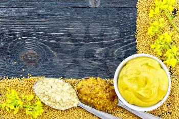 Frame of seeds and flowers of mustard, mustard sauce in a bowl, granular sauce and powder in spoons on the background of a black wooden board
