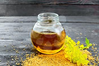 Mustard oil in a glass jar with flower and seeds on a wooden board background