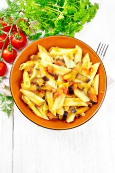 Penne pasta with eggplant and tomatoes in a bowl on towel, fork, garlic and parsley on a wooden plank background from above