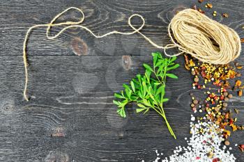 Sprig of fresh green rue with salt, pepper, fenugreek seeds and a coil of twine against a black wooden board