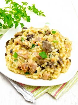 Rice risotto with mushrooms, chicken meat, cheese and garlic in a plate on a napkin, fork and parsley on a wooden board background
