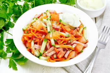 Salad from smoked sausage, spicy carrot, tomato, cucumber and spices with mayonnaise, towel, fork and parsley on a wooden board background