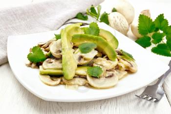 Salad of avocado and raw champignons, seasoned with lemon juice and vegetable oil with mint leaves, napkin and fork on wooden board background