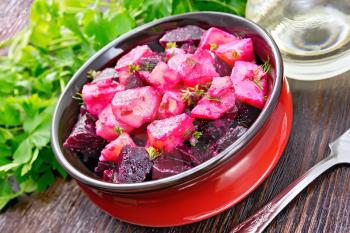 Beetroot and potato salad, seasoned with vegetable oil and vinegar in a bowl, parsley, fork on a brown wooden board background