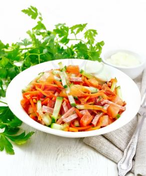 Salad from smoked sausage, spicy carrot, tomato, cucumber and spices with mayonnaise, napkin, fork and parsley on a light wooden board background