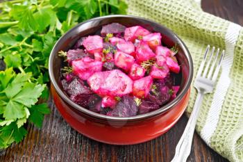 Beetroot and potato salad, seasoned with vegetable oil and vinegar in a bowl, parsley, napkin and fork on a wooden board background