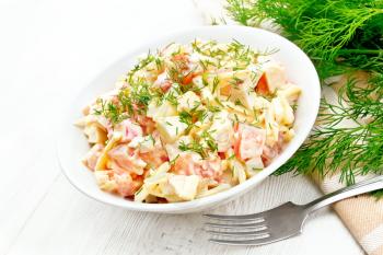 Salad of crab sticks, cheese, garlic, eggs and tomatoes, dressed with mayonnaise in a plate, napkin and parsley on the background of a light wooden board