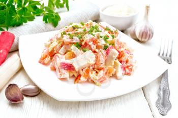 Salad of crab sticks, cheese, garlic and tomatoes, dressed with mayonnaise, towel and parsley on the background of a light wooden board