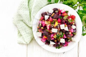 Salad with beetroot, feta cheese, apple, walnuts, parsley, seasoned with balsamic vinegar and olive oil in a plate, napkin against the background of a light wooden board on top
