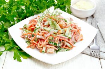 Salad from smoked sausage, spicy carrot, tomato, cucumber and spices, dressed with mayonnaise, towel, fork and parsley on a light wooden board background