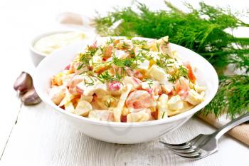 Salad of crab sticks, cheese, garlic, eggs and tomatoes, dressed with mayonnaise in a plate, kitchen towel and parsley on a wooden board background