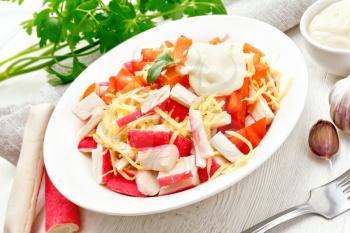 Salad of crab sticks, cheese, garlic and tomatoes with mayonnaise, towel, parsley on the background of a light wooden board
