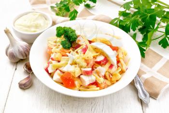 Salad of crab sticks, cheese, garlic, tomatoes and eggs with mayonnaise in a plate, towel, parsley and fork on a wooden board background